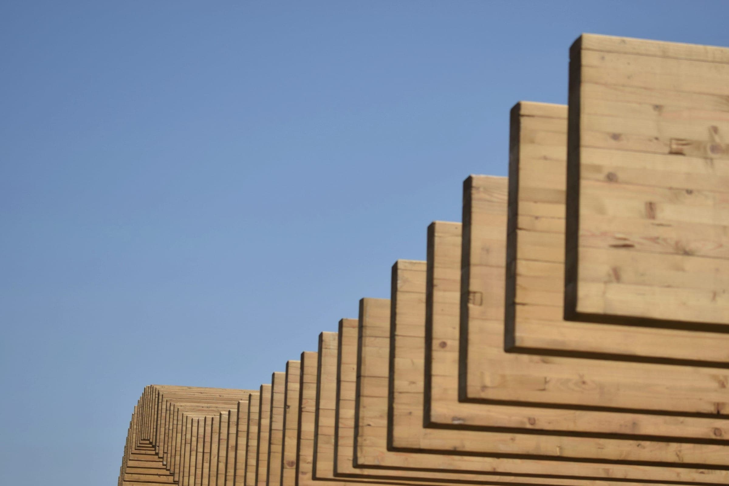 Laminated timber beams projecting in a repeating rhythm against a clear sky.